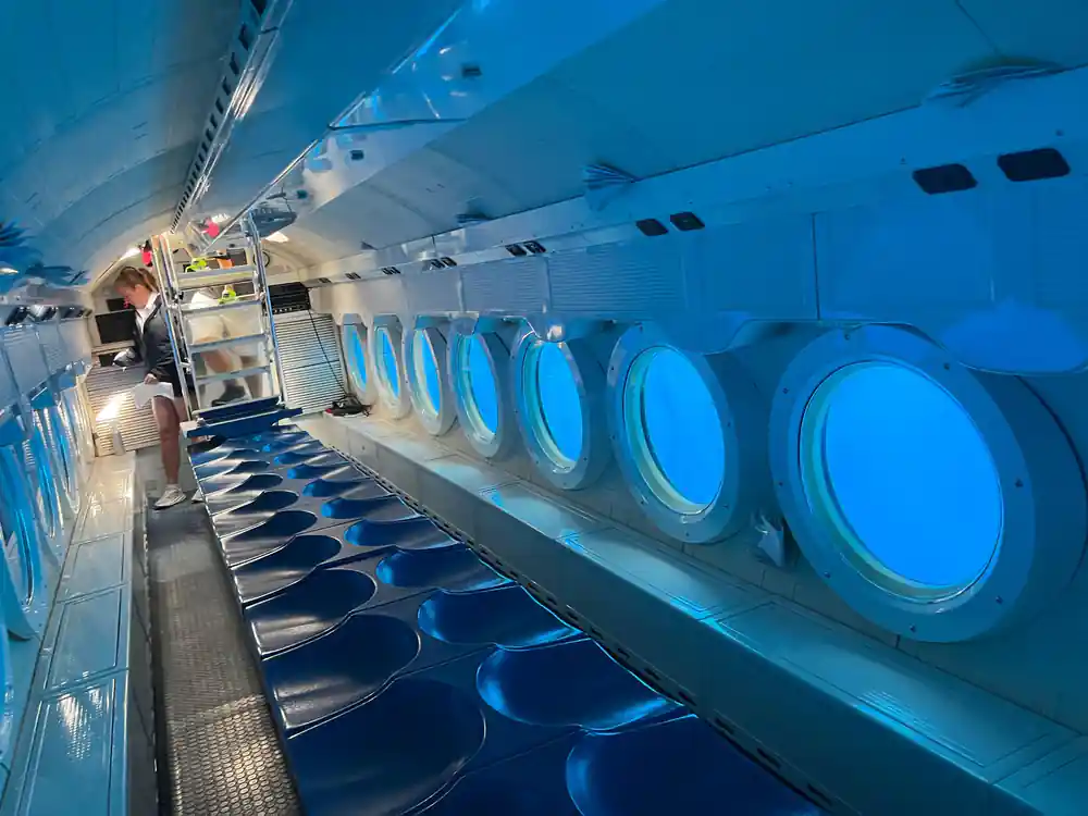 The full length of the cabin with blue bench seats and viewports
